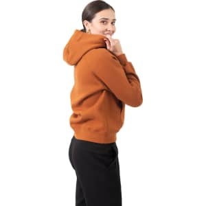 A woman smiles while wearing a burnt orange cotton hoodie with a kangaroo pocket and a logo.