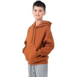 A hooded jumper in burnt orange colour featuring a kangaroo pocket and a logo. Worn with grey trousers.