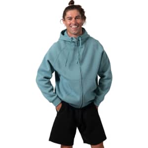 A man wearing a teal cotton zip-up hoodie with a kangaroo pocket and black shorts, smiling at the camera.