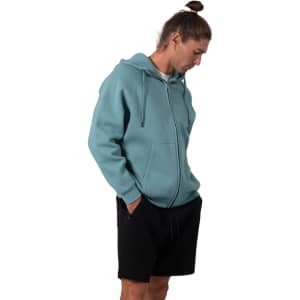 A men's cotton hoodie in teal with a kangaroo pocket and a zipper, worn with black shorts. The hoodie features a logo.