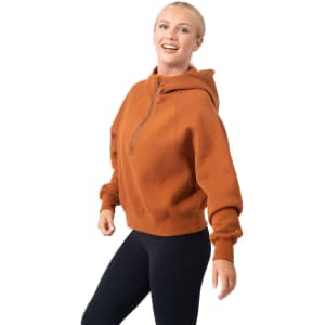 A half-zip jumper in a warm rust colour featuring a hood and a relaxed fit. Includes a logo on the garment.
