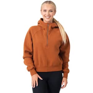 A woman wearing an orange half-zip cotton jumper with a hood, featuring a logo on the front.