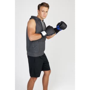 A man wearing a grey sleeveless hoodie, black shorts, and boxing gloves, posed for a promotional image.
