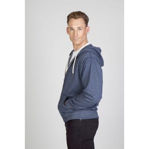A man wearing a navy blue heather zip hoodie, standing with his hands in the pockets and smiling.