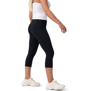 Black high-rise 3/4 leggings displayed on a model, paired with white sneakers. The image features a logo.