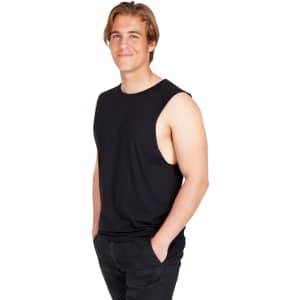 A man wearing a black combed cotton tank top, standing with hands in pockets and smiling. The tank has no sleeves and a relaxed fit.