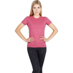 A woman stands with hands on hips, wearing a pink marl T-shirt and black jeans. The shirt has a logo.