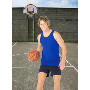 A man in a blue cotton singlet holds a basketball on an outdoor court with a grey wall in the background.