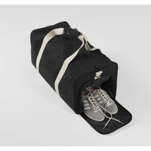 A black duffle bag featuring a white strap, with a pair of grey shoes visible inside. The bag has a logo.