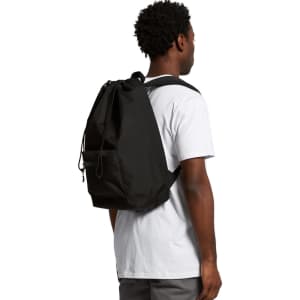 A black recycled rucksack is worn on the back of a person, featuring a simple design with adjustable straps.