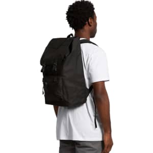 A black recycled field backpack is worn on the back of a person in a white t-shirt. The backpack has adjustable straps and a logo.
