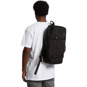 A black recycled strap backpack is worn on the back of a person, who is facing away, dressed in a white t-shirt.