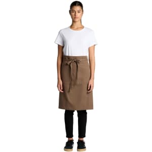A woman wearing a brown canvas half apron over a white t-shirt and black pants, with a branding logo present.