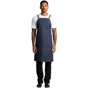 A denim apron featuring tan straps, worn by a person standing upright against a white background.