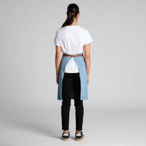 A denim half apron in blue, worn over black pants, with a brown belt detail at the back.