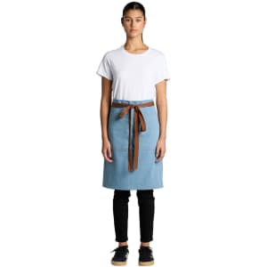 A denim half apron in light blue with a brown waist tie, displayed on a model wearing a white T-shirt and black pants.