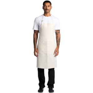 A man wearing a beige linen apron over a white t-shirt and black pants, featuring a logo.