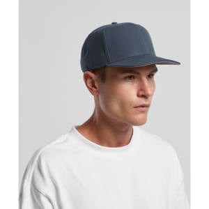 A blue cap with a flat brim, featuring a logo on the front, worn by a model in a white t-shirt.