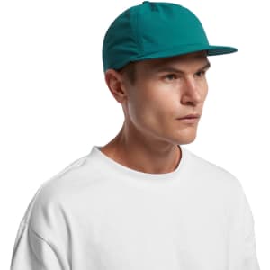 A teal cap with a flat brim and a branded logo on the front, worn by a model in a white shirt.