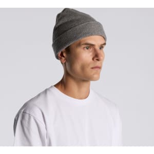 A grey knit beanie is worn by a model with short hair, dressed in a plain white t-shirt. The beanie has a logo.