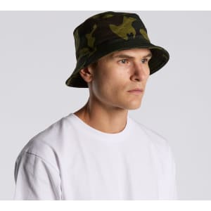 A camo bucket hat in green and black patterns, worn by a model facing sideways. Features a logo on the hat.