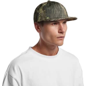 A camo cap in shades of green and brown, featuring a flat brim and a structured design, worn by a model.