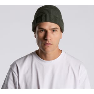 A green beanie worn by a person in a white t-shirt, featuring a subtle logo.