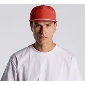 A red cap with a flat brim is worn by a model in a plain white T-shirt. The cap features a logo on the front.