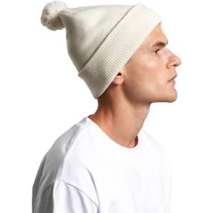 A light cream pom pom beanie worn by a person, featuring a fluffy top and ribbed texture.