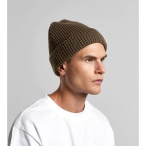A green ribbed beanie is worn by a model, showcasing its textured design and fitted style.