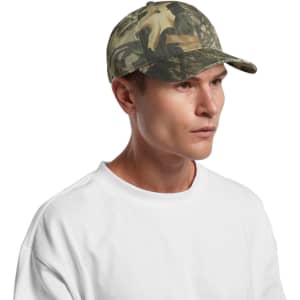 A camo cap in shades of green and brown, featuring a curved brim and a logo on the side, worn by a man.