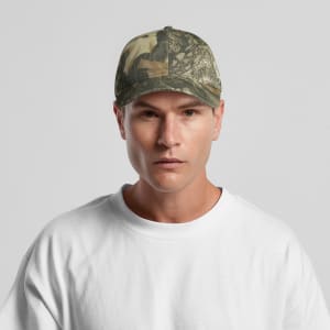 A camo cap featuring a mix of green and brown patterns, worn by a model in a white t-shirt. The cap has a logo.