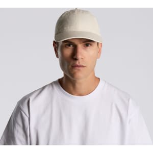 A beige cap worn by a model, featuring a front-panel design and a logo. The model is dressed in a white T-shirt.