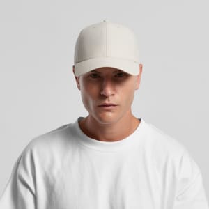 A light beige nylon cap displayed on a model wearing a white sweatshirt. The cap features a logo.