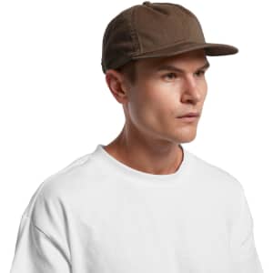 A brown cap with a curved brim, worn by a model in a white t-shirt. The cap features stitching details and a logo.