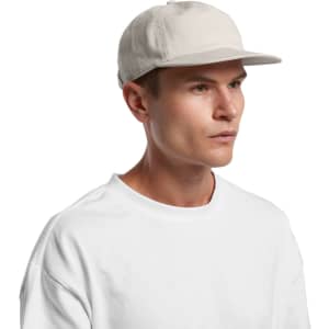 A light beige panel cap worn by a person, featuring a flat brim and a logo on the side.