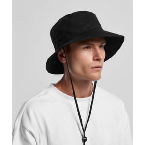 A black wide brim bucket hat with a chin strap, worn by a person in a white t-shirt.