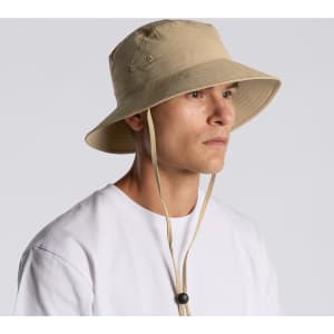 A beige nylon wide brim bucket hat with a chin strap and ventilation holes, displayed on a model.