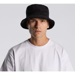 A black cord bucket hat worn by a model, paired with a plain white t-shirt. The hat features a branding logo.