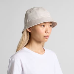 A cream-coloured bucket hat with a wide brim, featuring a stitched design and a subtle logo.