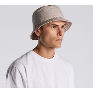 A beige bucket hat worn by a model, featuring stitching details and a visible brand logo.