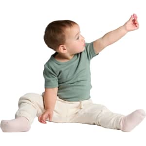 A seated infant wearing a green organic t-shirt and light-coloured trousers, reaching out with one hand.