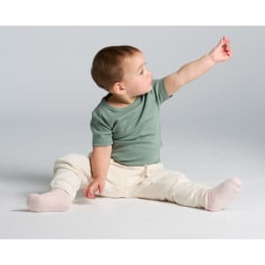 A baby wearing a green organic cotton T-shirt and cream-coloured pants, reaching out with one hand.