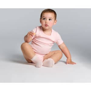 A pink Organic Infant Mini-Me One-Piece displayed on a seated toddler, featuring a simple design and soft fabric.