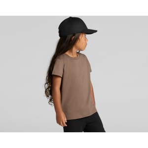 A brown kids' t-shirt displayed on a child, paired with a black cap, featuring long hair and a side profile.