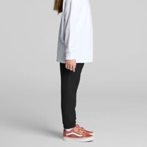 A child wearing black track pants with a white long-sleeve top and pink patterned shoes, standing sideways.