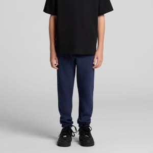 Youth Supply track pants in navy blue, styled with a black T-shirt and black sneakers. Features a logo.