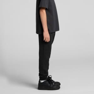 Black youth track pants displayed on a person, paired with a matching dark shirt and black shoes. Features a logo.