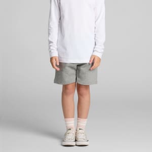 Kids grey stadium shorts displayed on a child wearing a long-sleeve white shirt and light-coloured shoes.