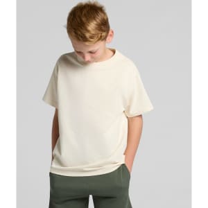 A youth classic tee in cream colour, featuring a relaxed fit and short sleeves. The model stands with hands in pockets.